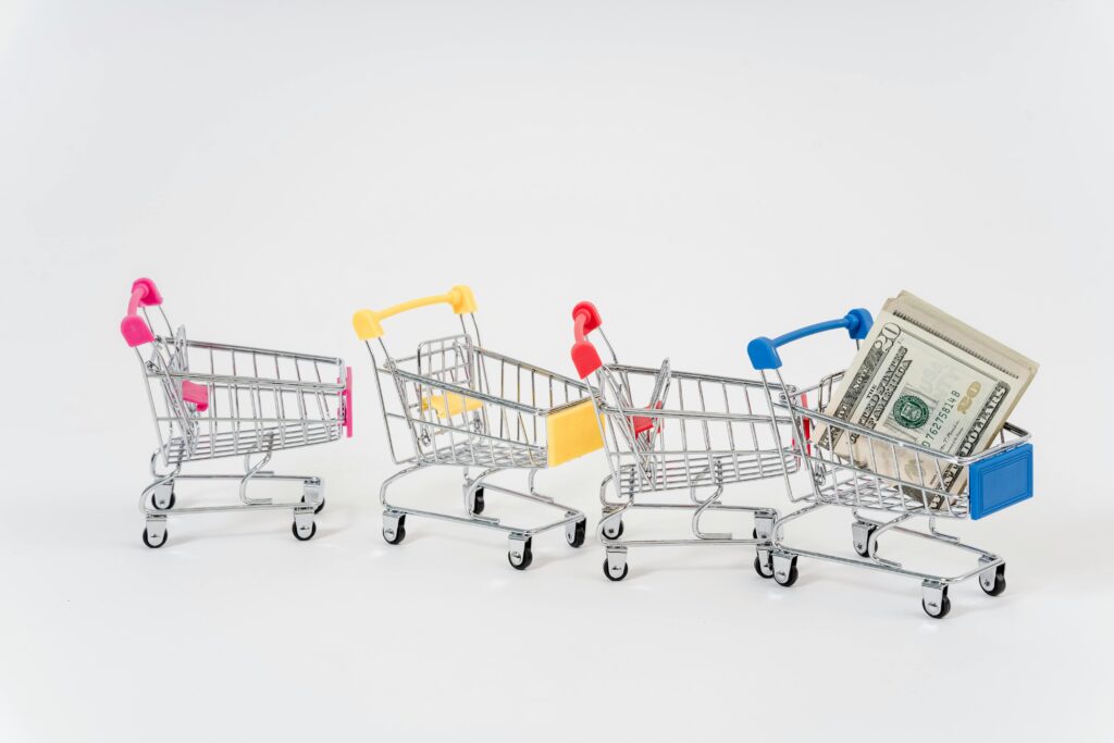 Miniature shopping carts in bright colors with dollar bills imply financial shopping themes.