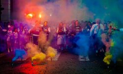 A lively group celebrating at night with color smoke bombs in a street festival.